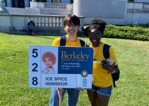 Two Orientation Leaders holding a Golden Guidepost depicting a fake Cal 1 Card belonging to Ice Spice